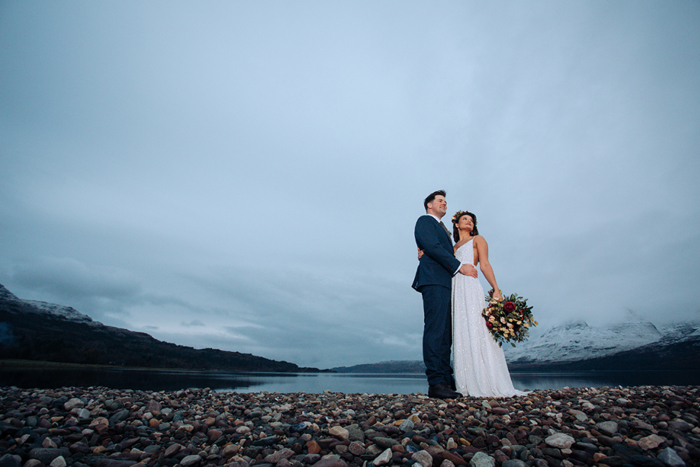 Bride and groom hold each other in front of a dramatic Highland backdrop 