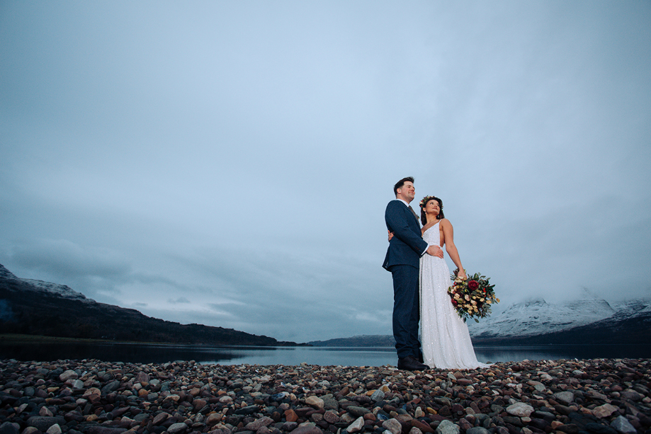 Bride and groom hold each other in front of a dramatic Highland backdrop