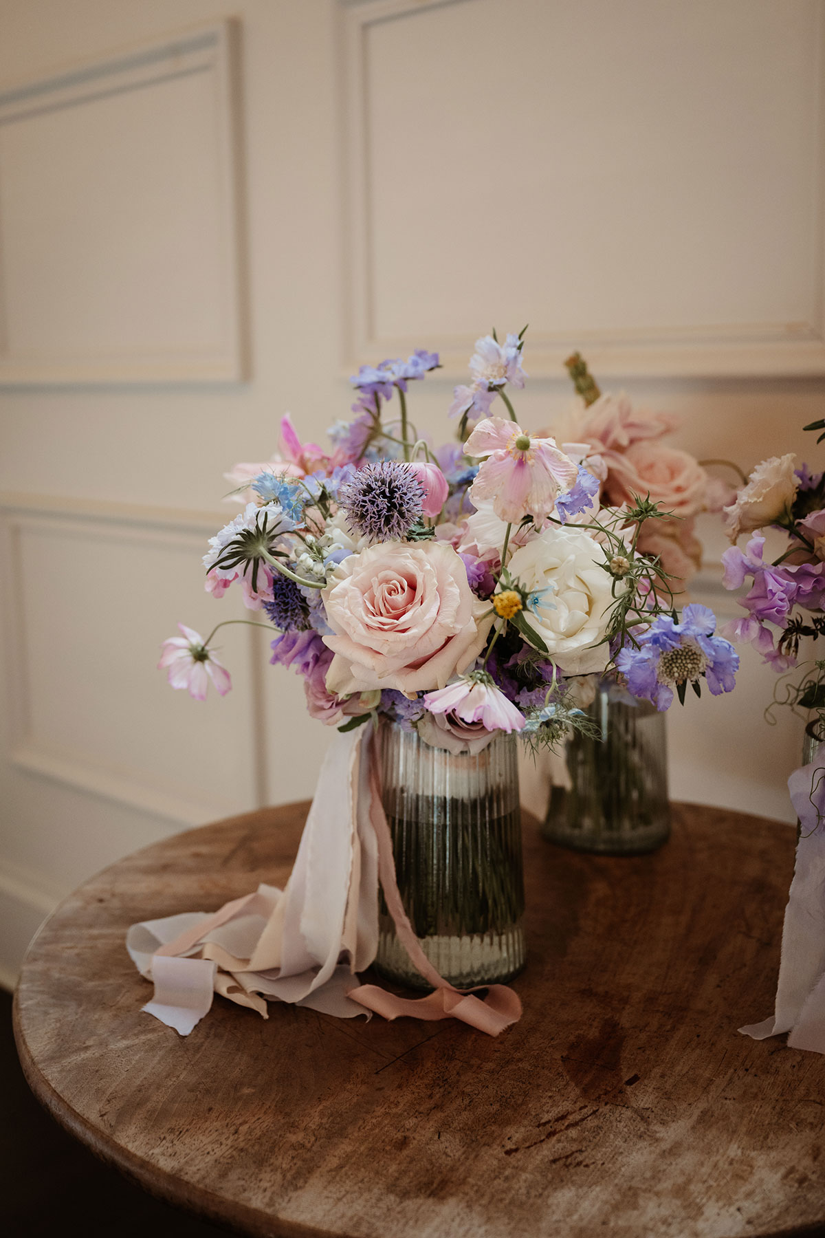 a pastel bridal bouquet in a glass vase on a wooden table