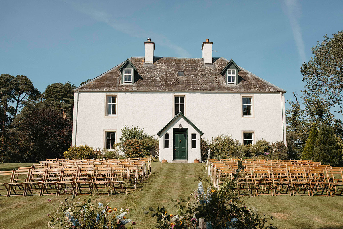 Rows of wooden chairs arranged on lawn for outdoor Highland wedding ceremony at family farmhouse in Nethy Bridge