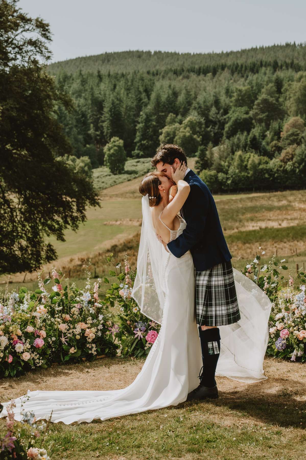 Newlyweds kiss beside colourful floral arrangements during their outdoor Ballogie House wedding