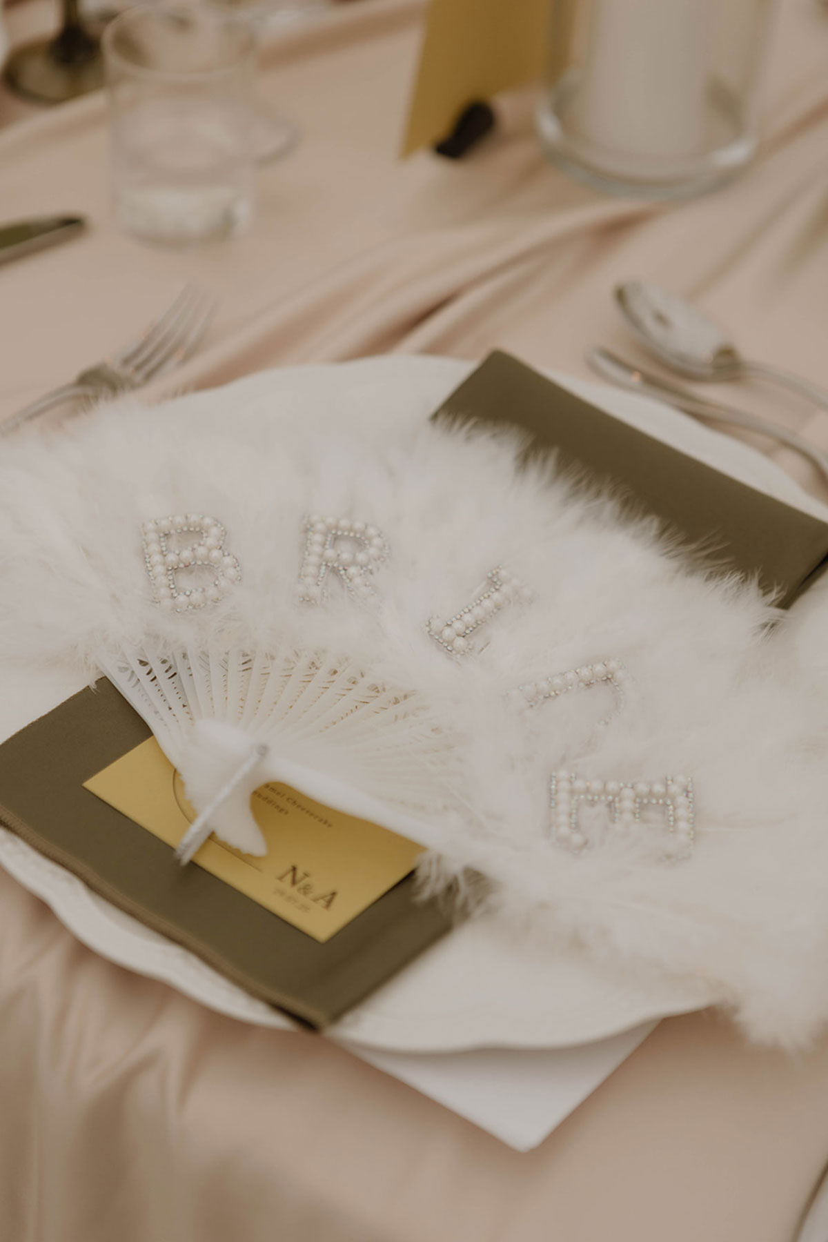 Bridal feather fan place setting detail with pearl lettering at luxury marquee wedding reception in Ayrshire