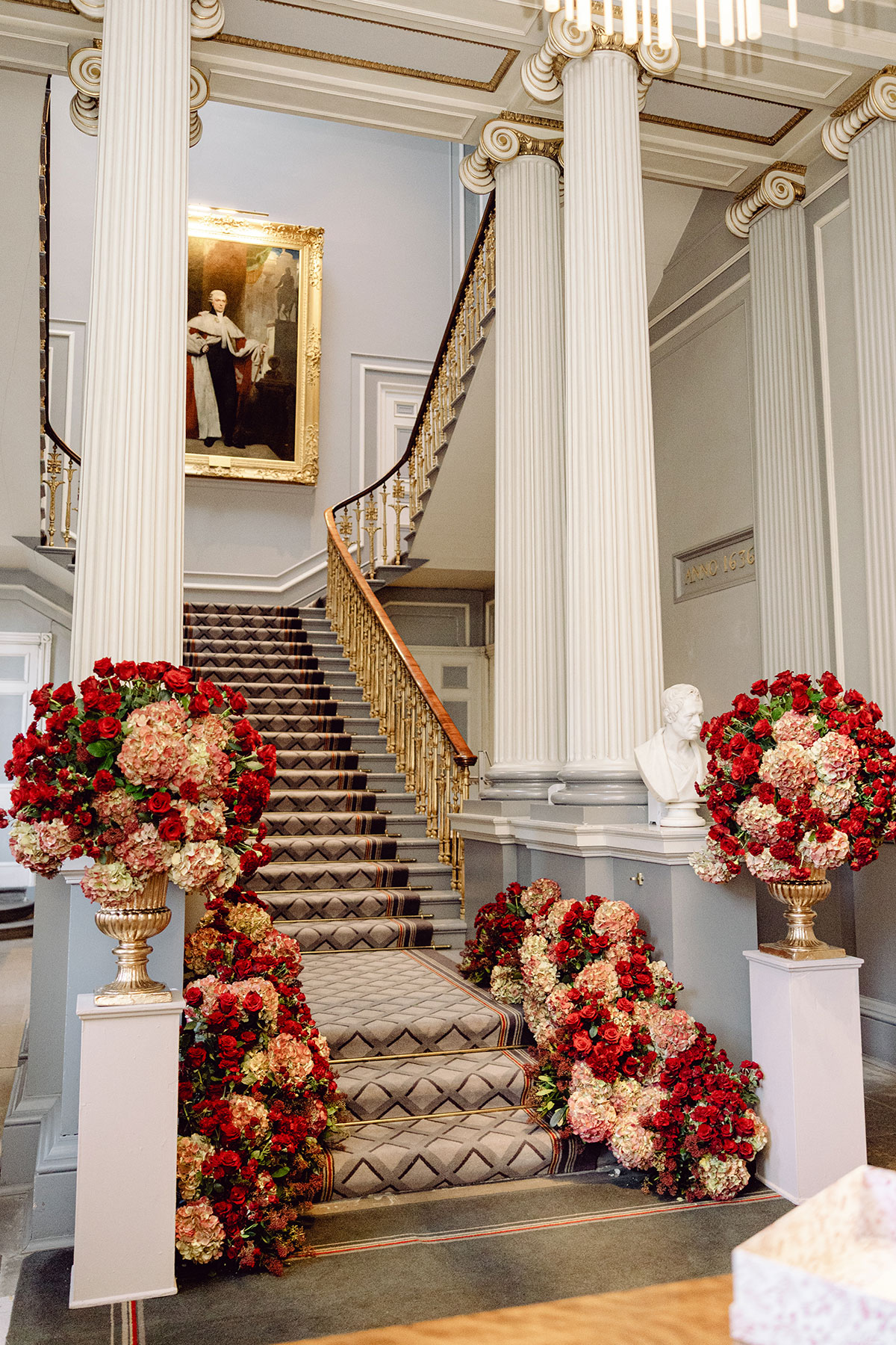 Grand staircase at The Signet Library decorated with large red and blush floral arrangements