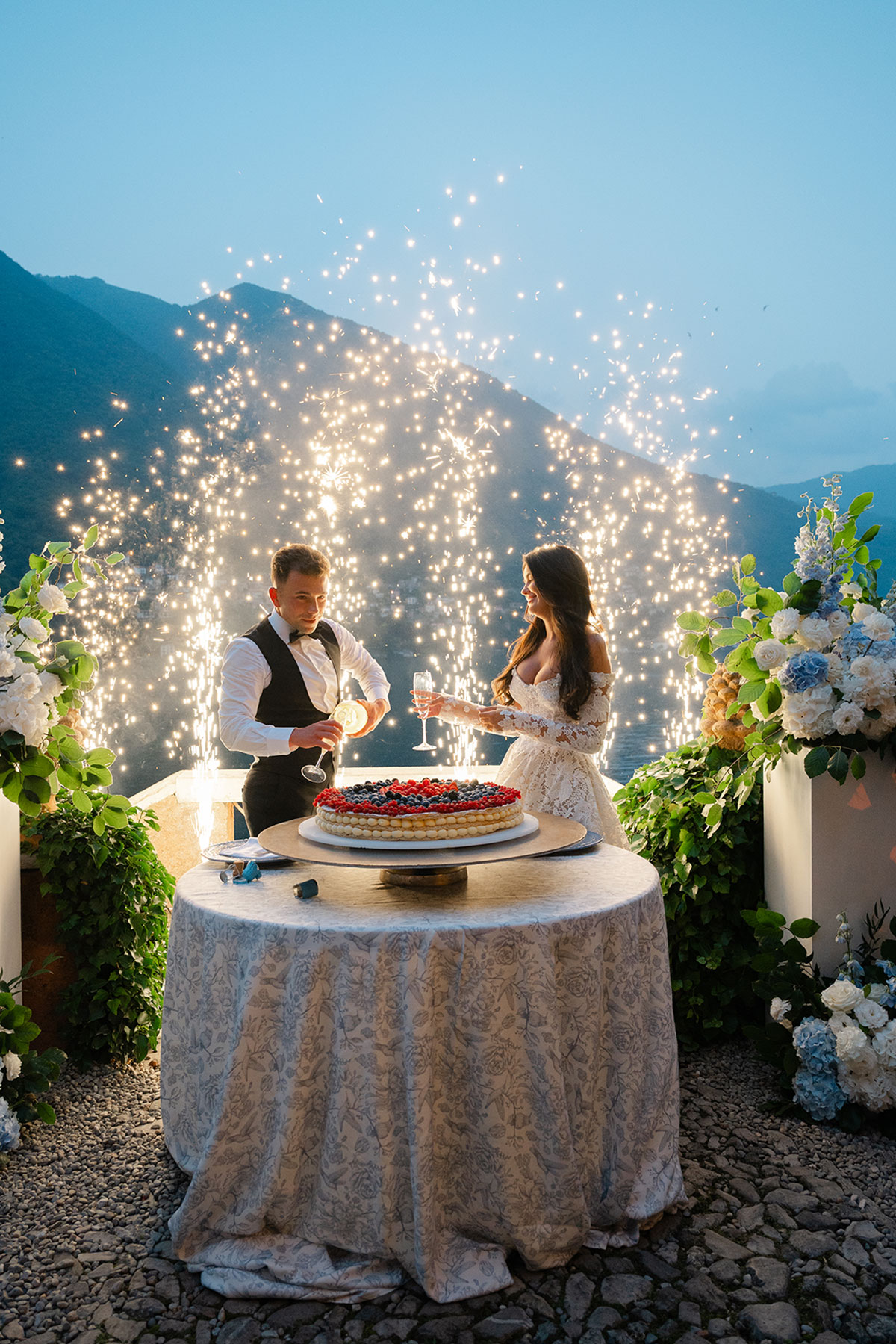 Bride and groom cutting a millefoglie wedding cake as pyrotechnic sparklers light up the Lake Como evening.