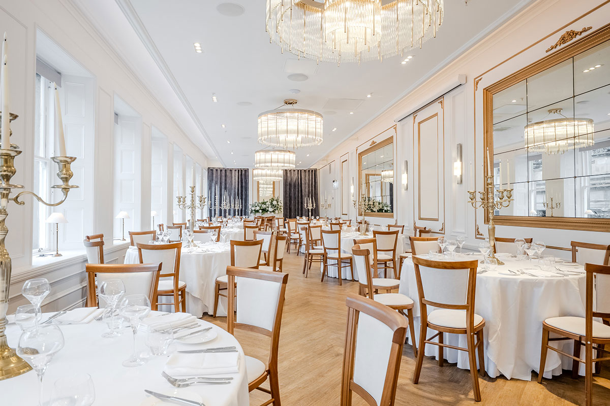 round white tablecloth tables with brown and cream chairs set around them and tall gold candelabras set in the middle of each