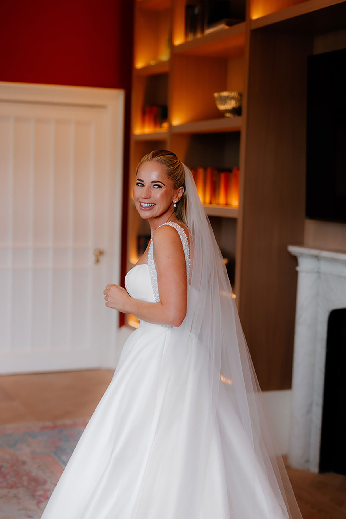 Bride smiling in her wedding dress and veil inside Mar Hall, standing near bookshelves and warm lighting.
