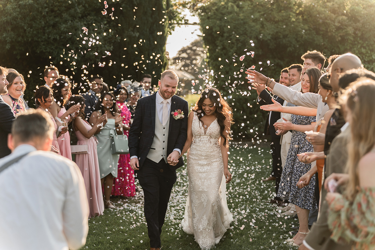 Newly married couple walking while guests throw confetti 