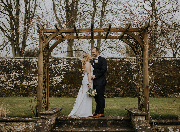 A bride and groom look into each other's eyes as they stand under a pergola