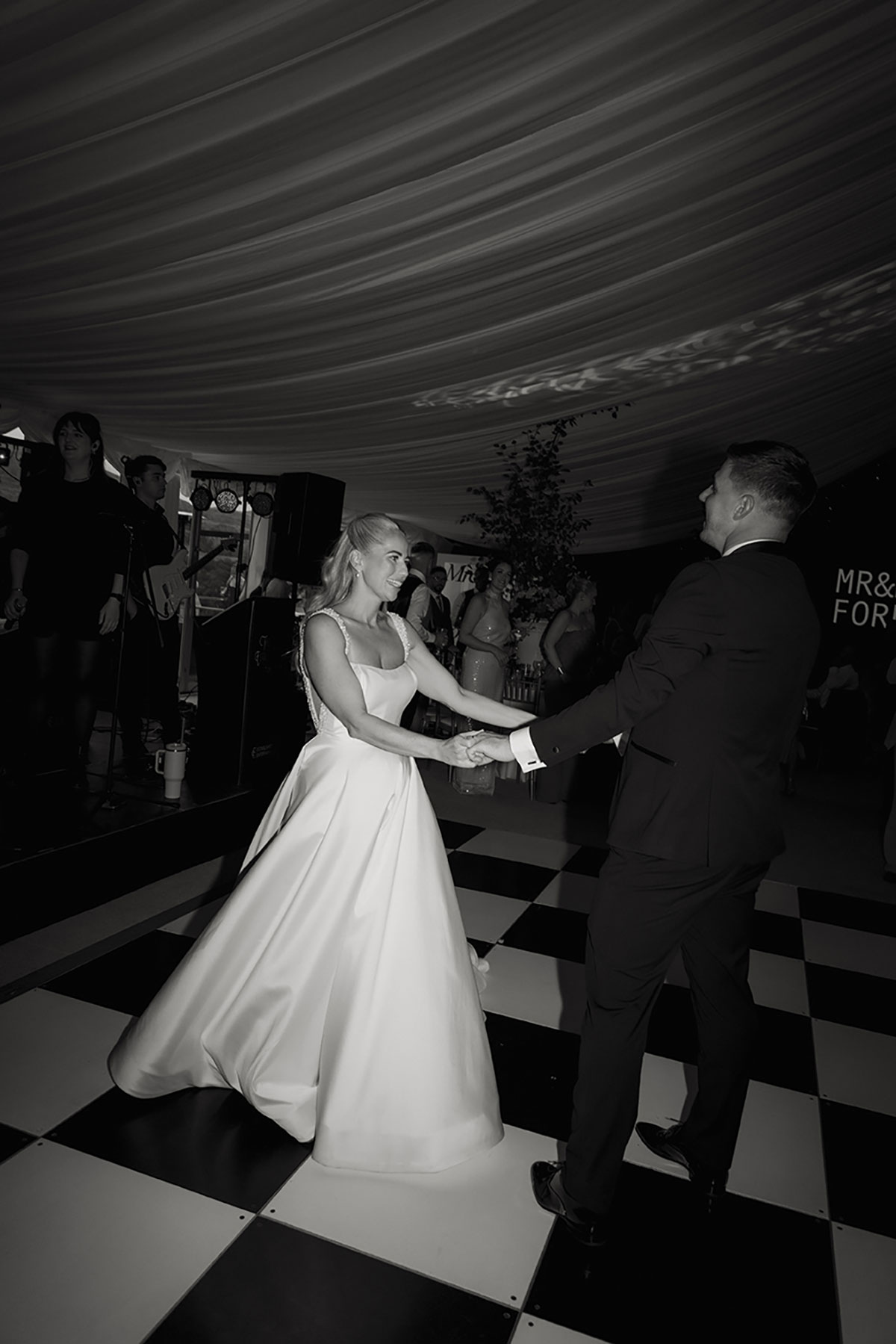 Black-and-white photo of the couple enjoying their first dance on a black-and-white chequered dancefloor.