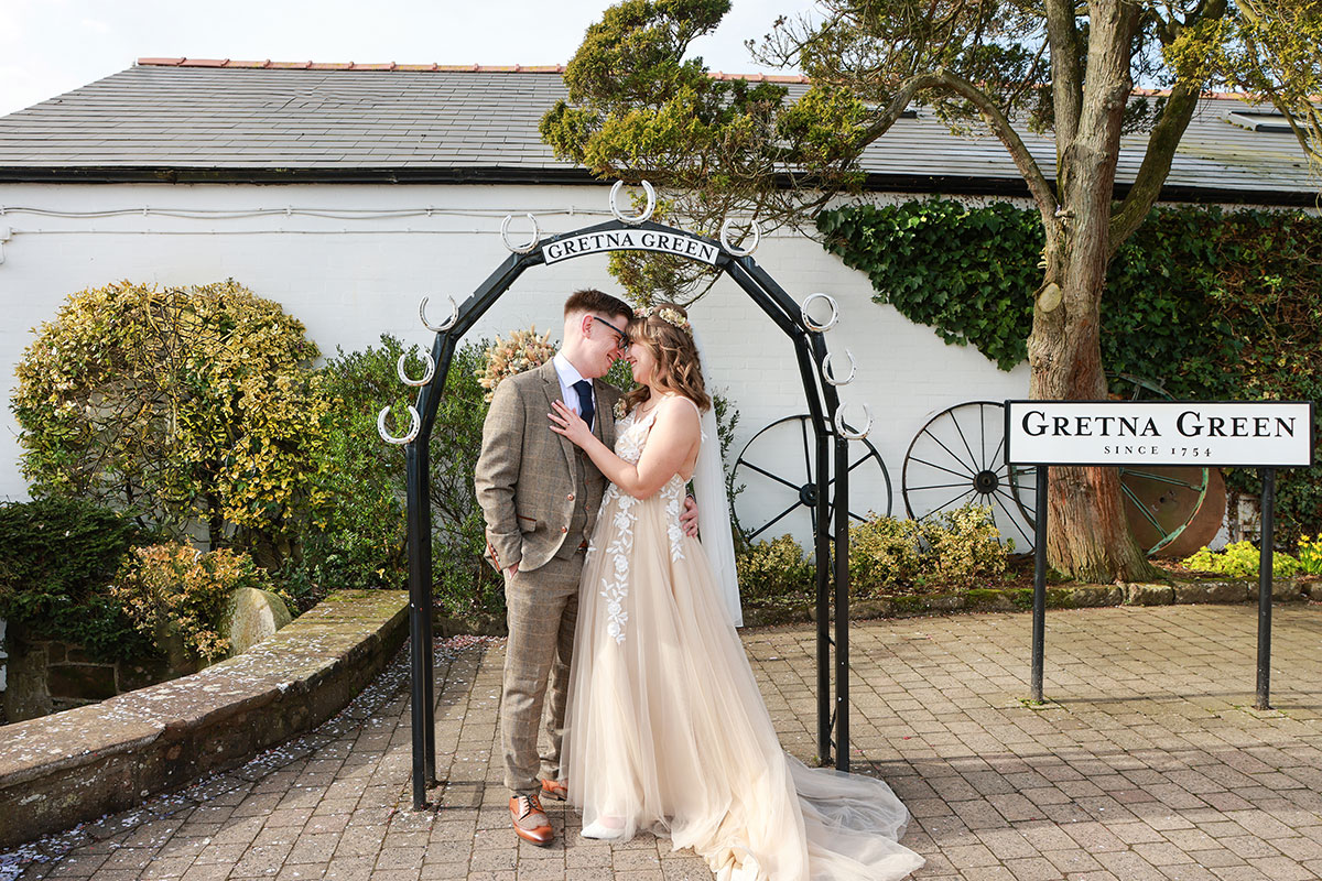 bride and groom smile at one another underneath black metal archway at gretna green