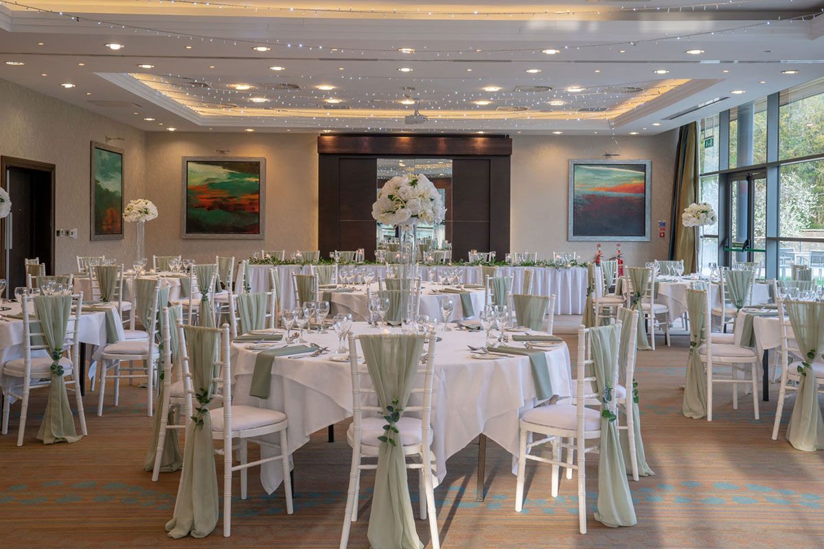white tablecloth round dining tables set up in formal room accompanied by white chairs with green drapes hanging off the back 