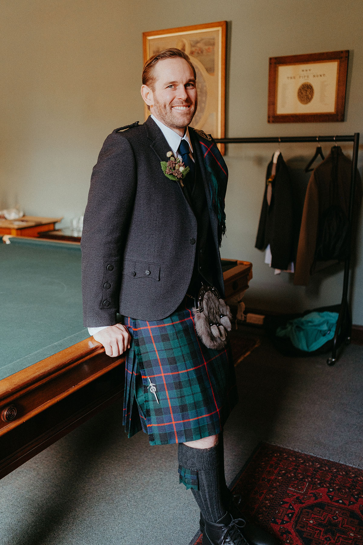 Groom wearing a traditional Scottish kilt poses in the Billiards Room at Cambo Country House before the wedding ceremony.