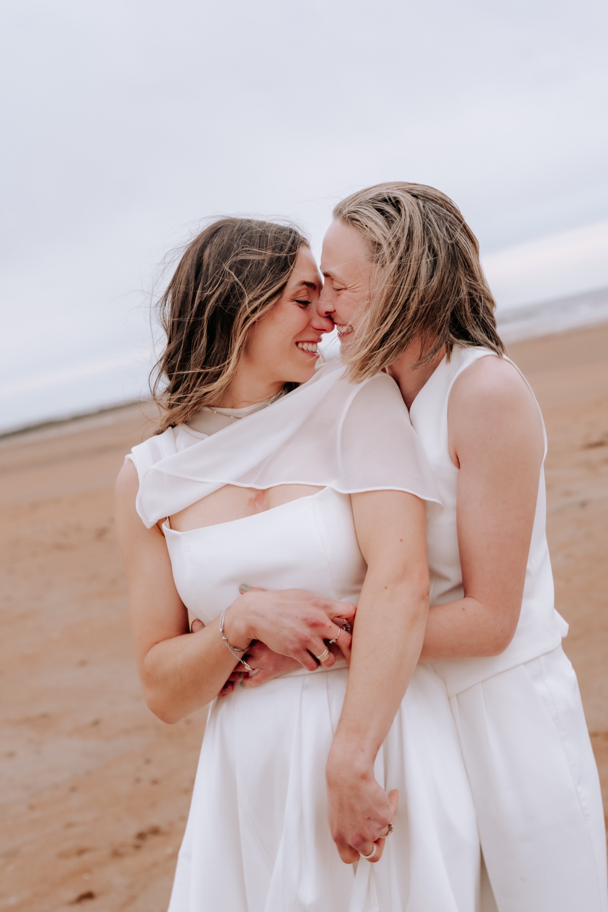 Hannah and Donna embracing and smiling together during their beach wedding portraits.