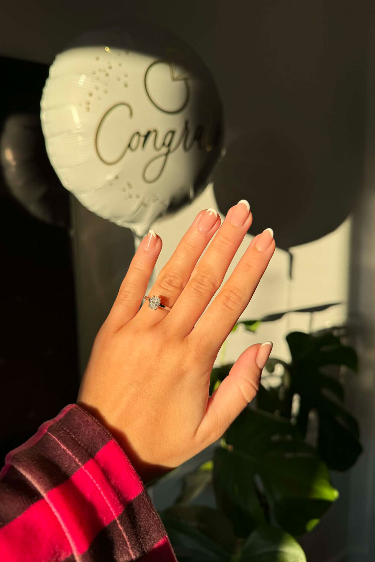 close up of engagement ring on hand with neutral manicure and congratulations balloon in background
