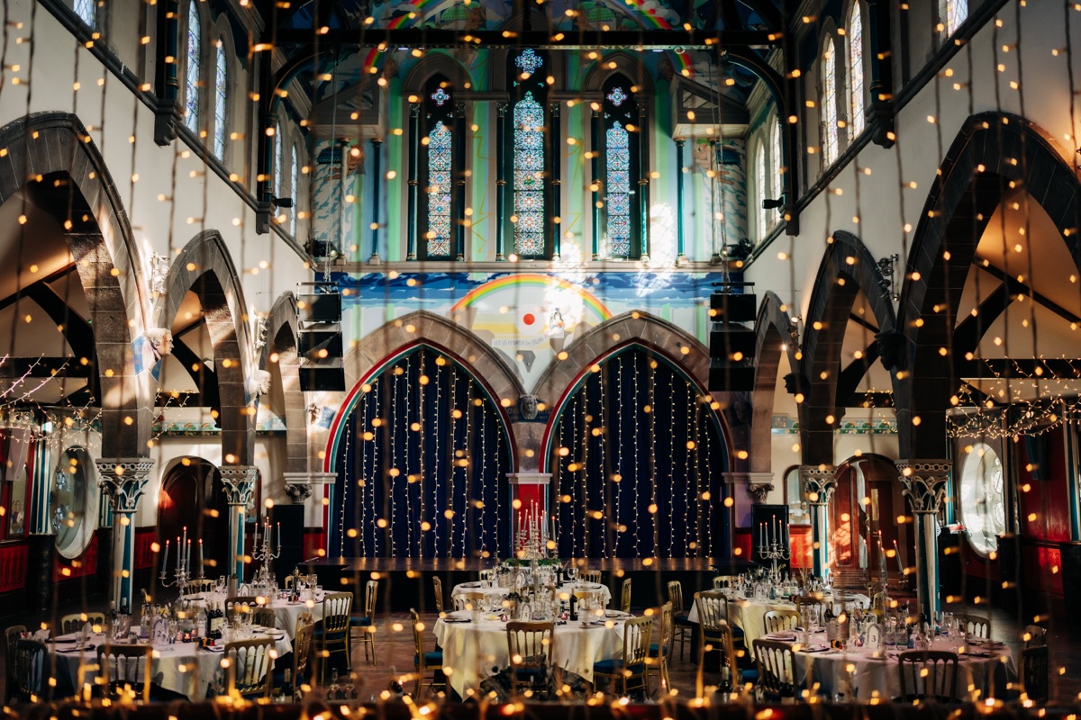 Òran Mór's Auditorium set up for a Glasgow wedding reception, with round dining tables, fairy lights, candelabras and colourful ceiling artwork