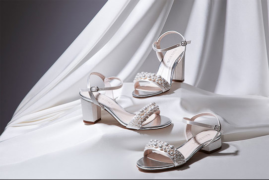 Three white sandals with different height of heels and pearls attached to the front strap across the shoe