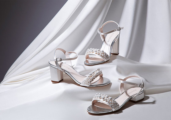 Three white sandals with different height of heels and pearls attached to the front strap across the shoe