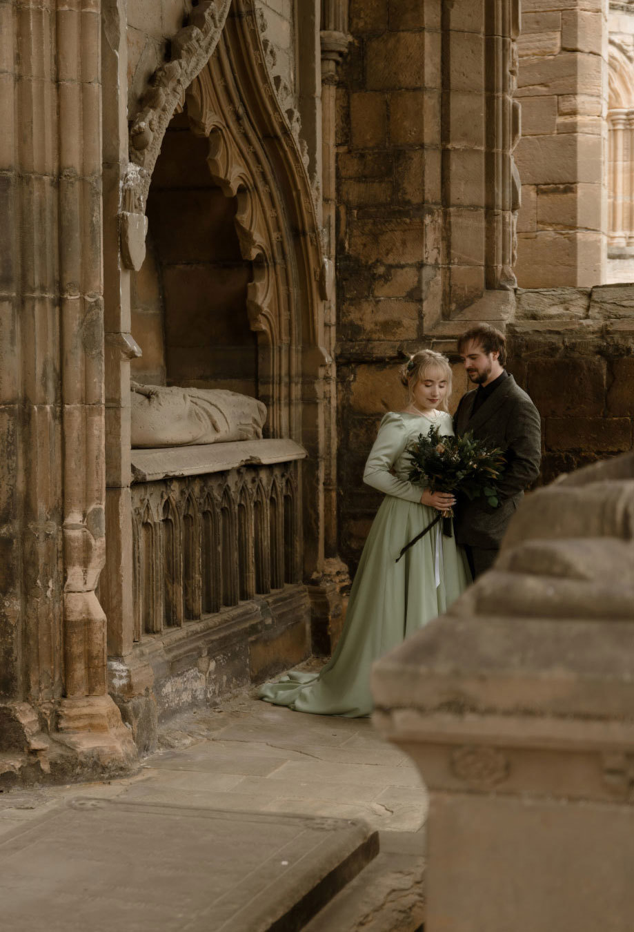 A bride and groom stand closely together in a quiet, historic corner of Elgin Cathedral