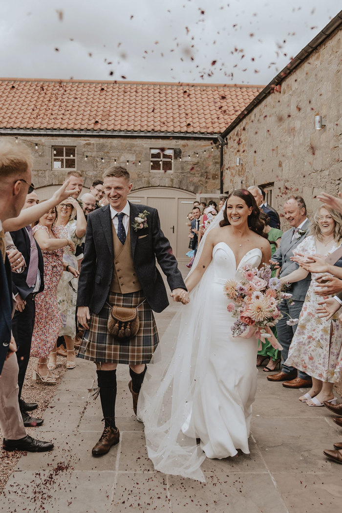 bride and groom walk outside as guests throw confetti over them