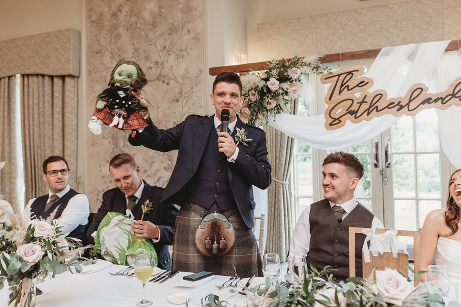 Best man holds doll during wedding speeches