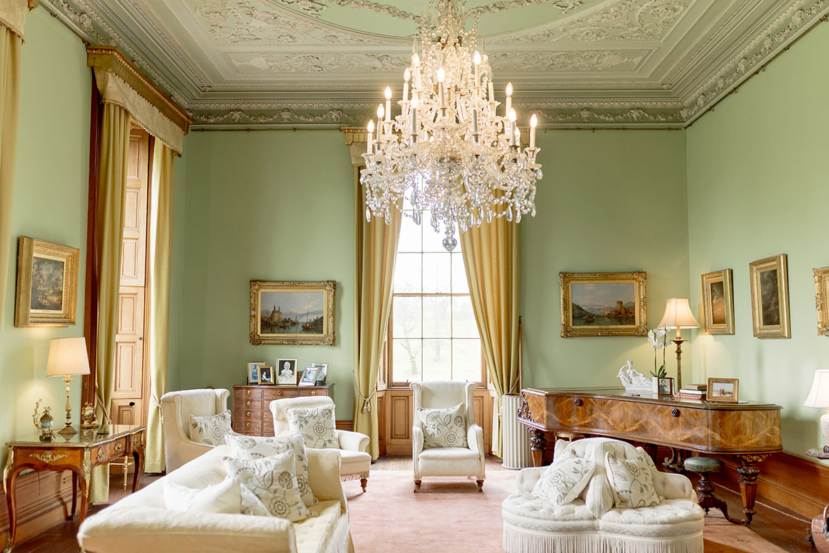 Elegant drawing room at Cluny Castle featuring a crystal chandelier, grand piano, period furnishings and tall windows