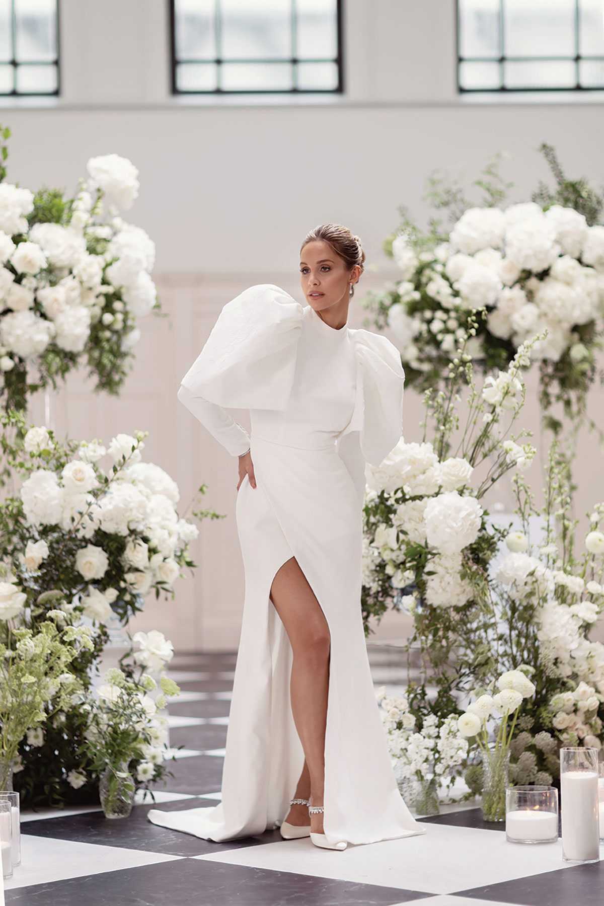 Bride posing in high-slit white gown with puff sleeves, surrounded by white hydrangeas and roses