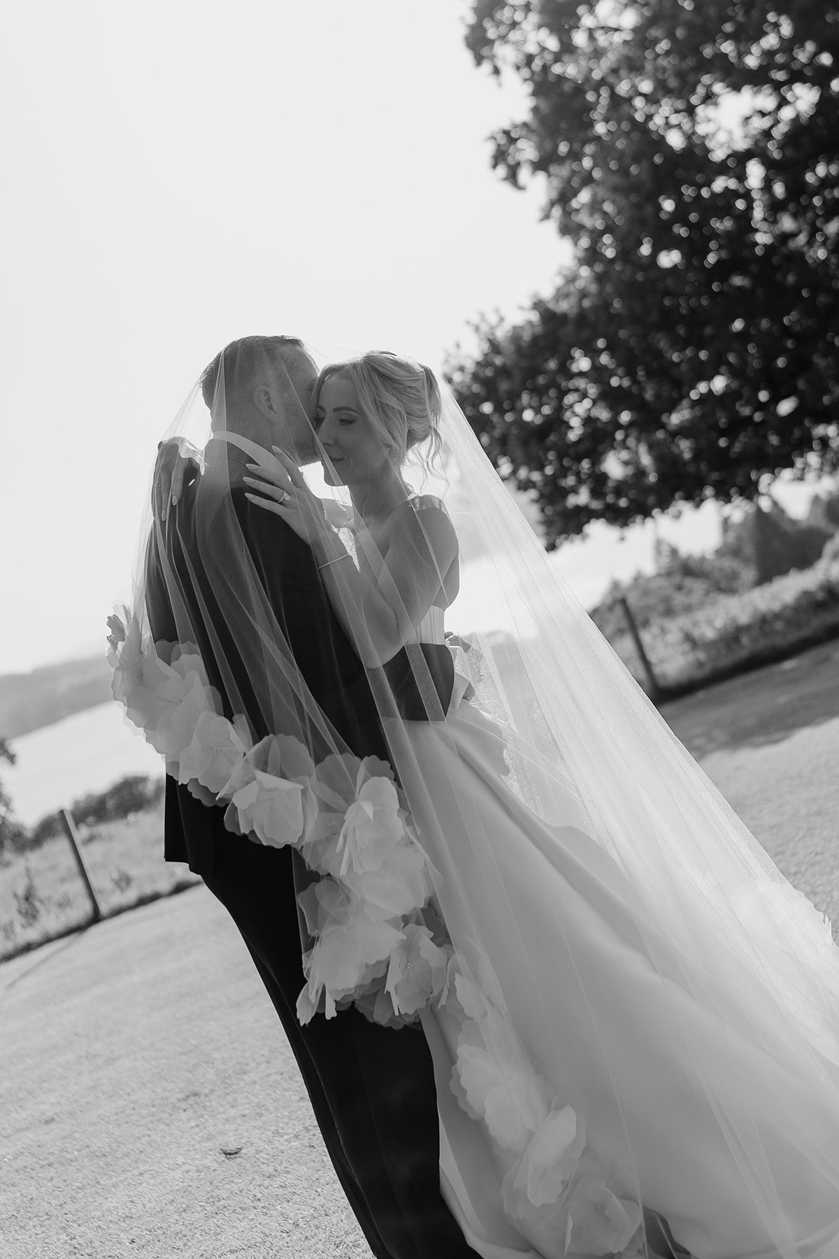 Black and white portrait of the bride and groom embracing beneath the bride's floral-edged veil at their Boturich Castle wedding.