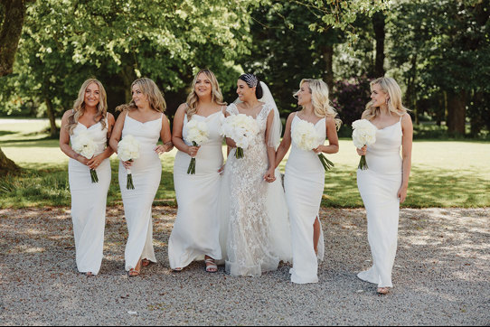 A bride and her five bridesmaids, who are all dressed in white, walk outside (photo: Sam Brill)