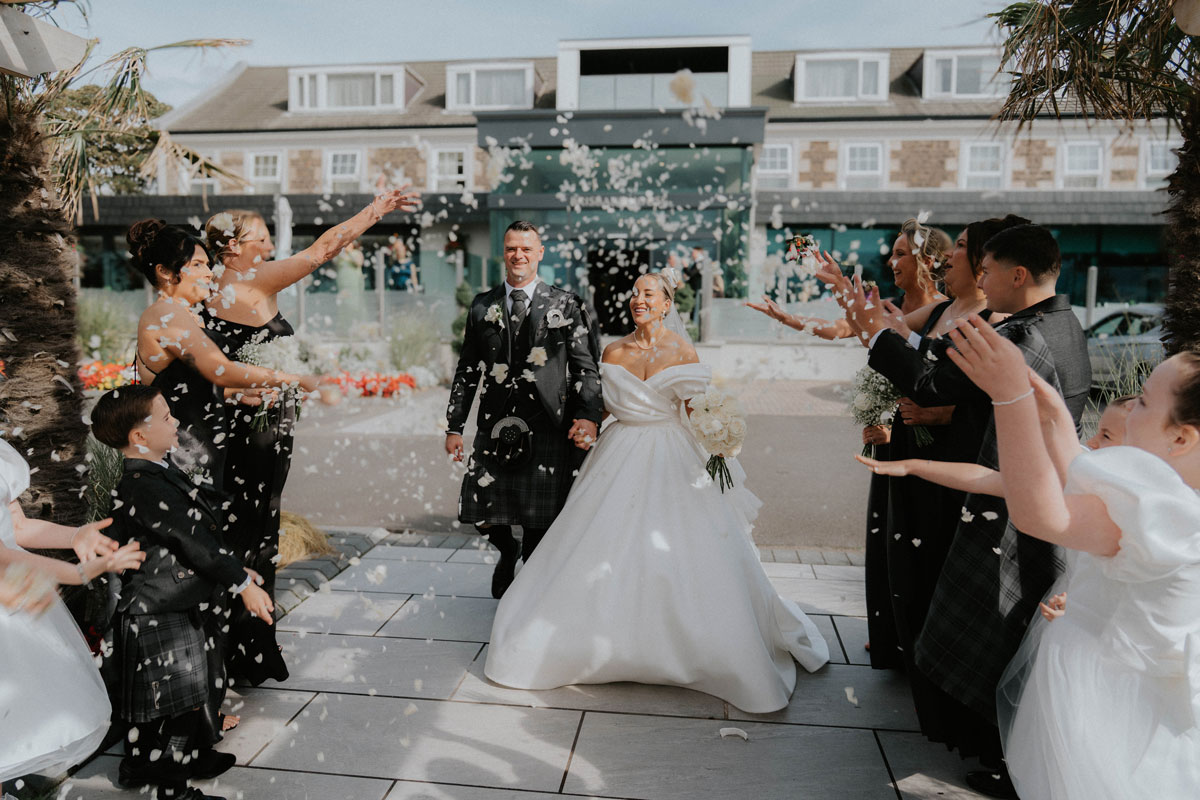 Bride and groom walking through confetti outside Brisbane House Hotel following church ceremony