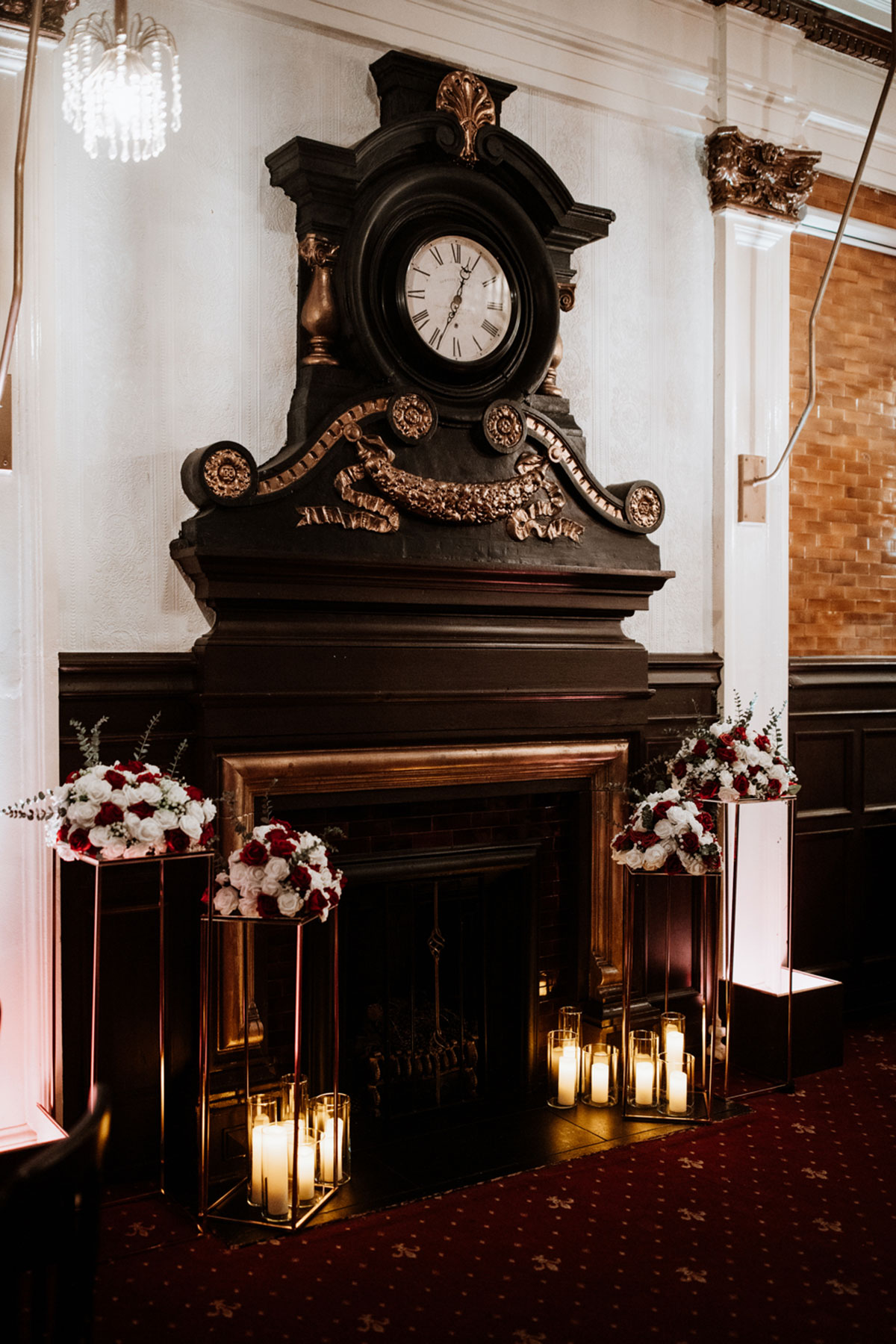 Ornate fireplace at The Savings Bank in Glasgow styled with red and white wedding flowers and candle lanterns.