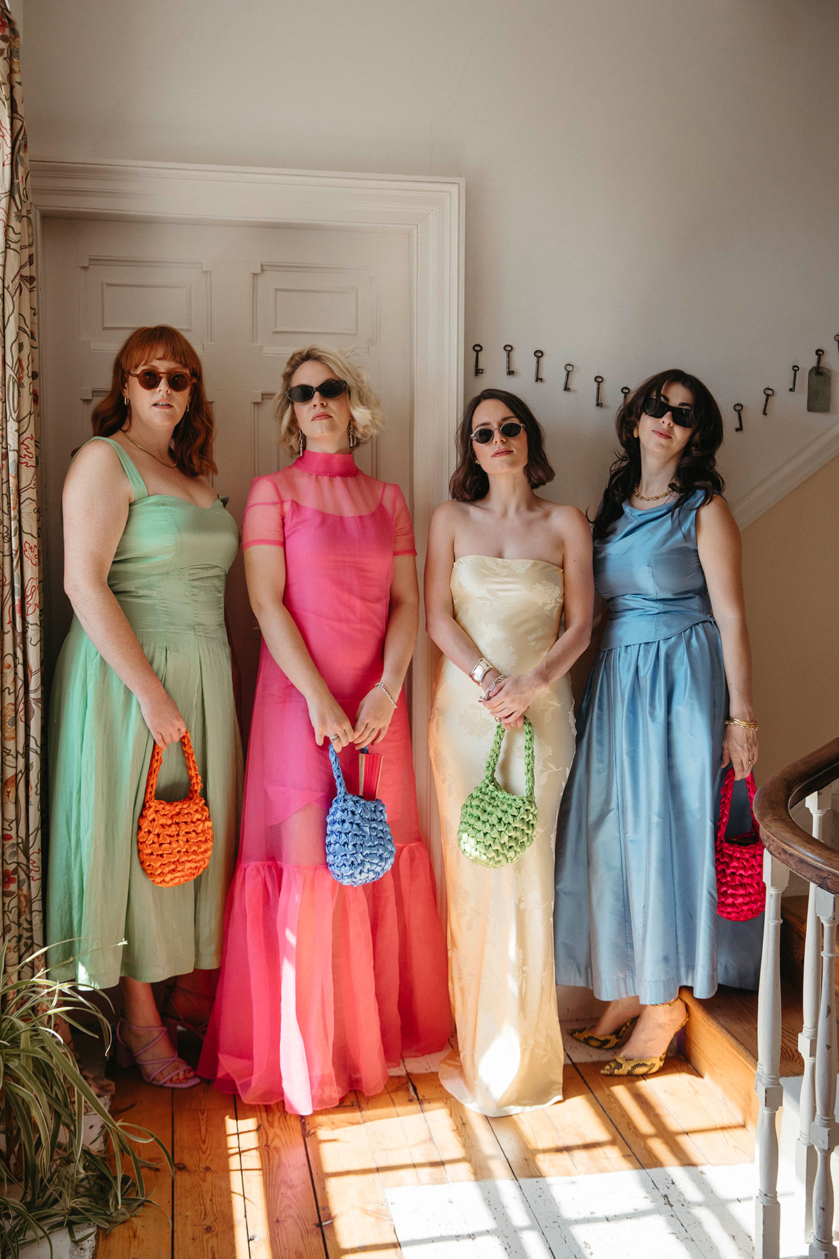 Wedding guests in colourful dresses with statement handbags posing on a staircase