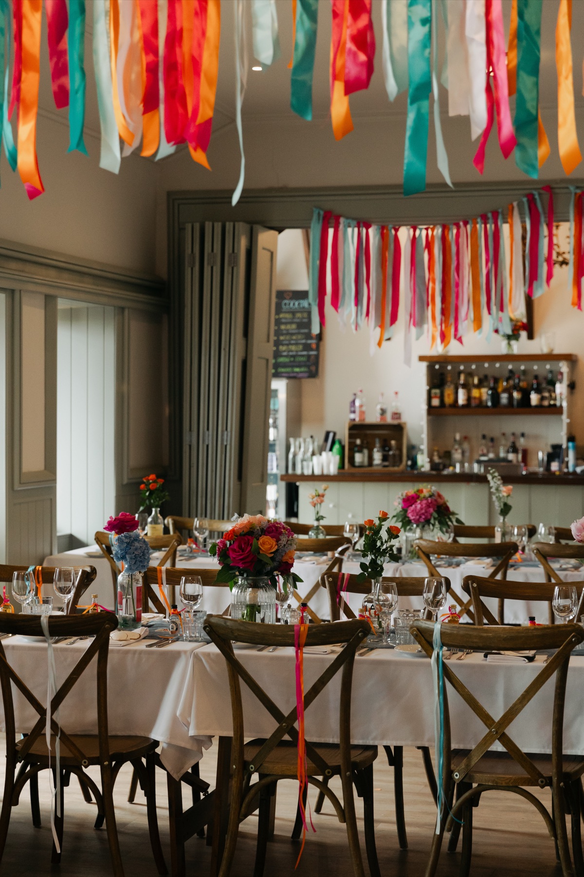 Colourful pink, orange, turquoise and white ribbon decorations hang above wedding reception tables at The Dougarie Boathouse.