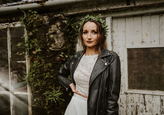 Bride wears black leather jacket over her dress and green foliage hair accessory