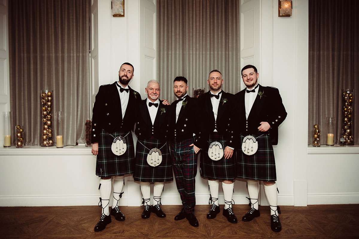 Group of men wearing formal jackets and kilts posing indoors for a portrait