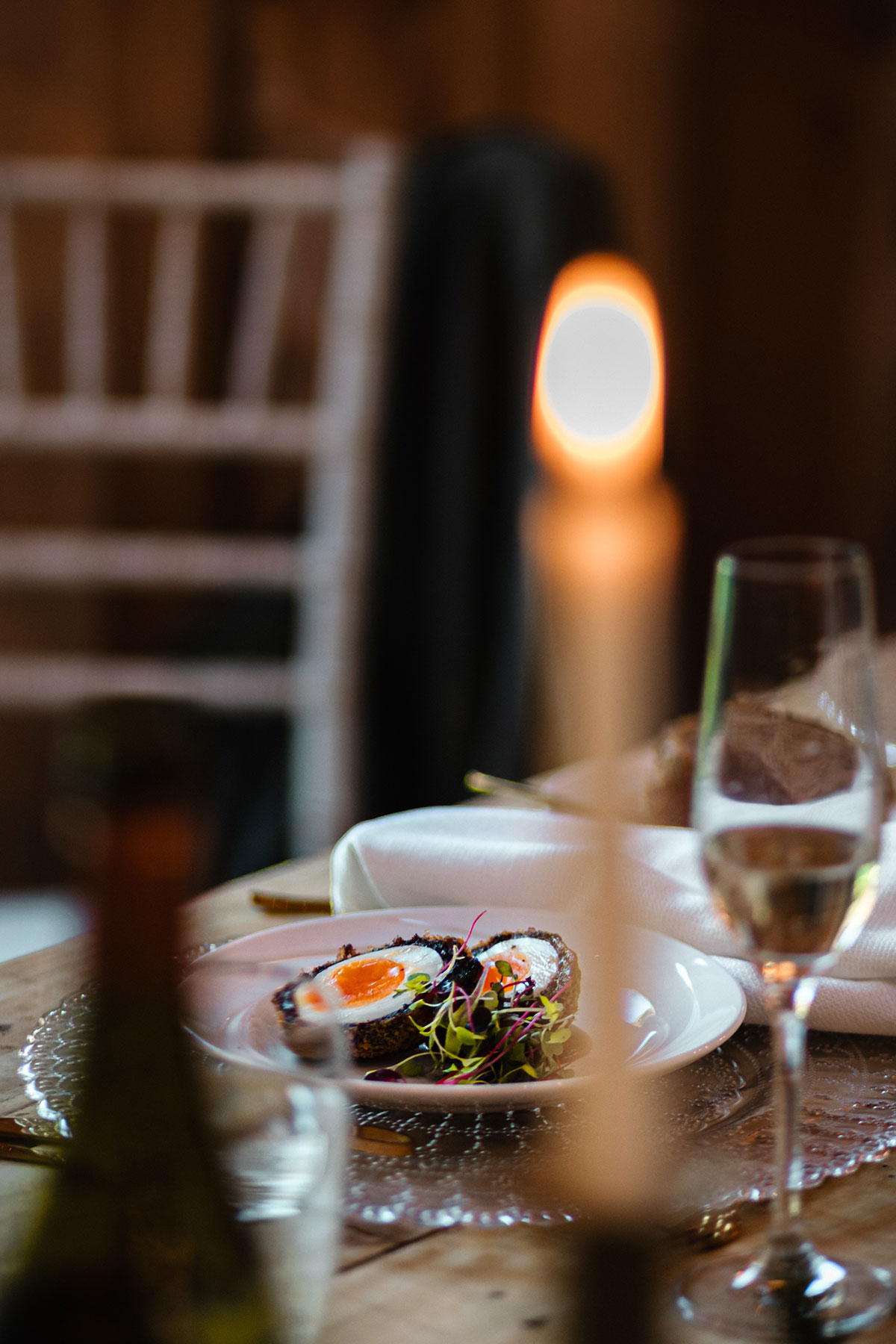 A plated starter featuring a halved Scotch egg with vibrant orange yolk and micro herbs, set on an elegantly dressed wedding dining table