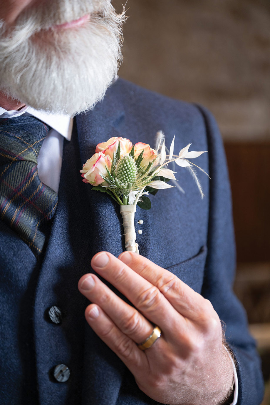 a tartan tie, blue tweed jacket and hand on a thistle and rose buttonhole