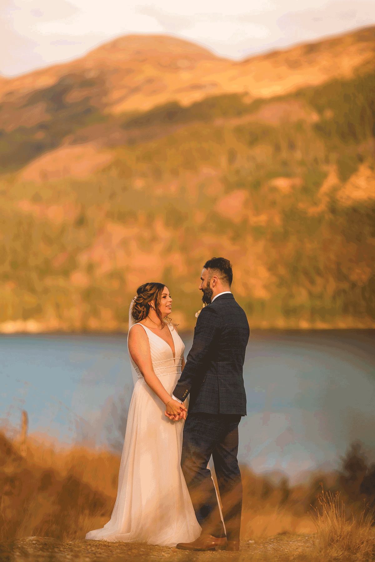 Bride and groom holding hands and facing one another, outdoors, golden hour