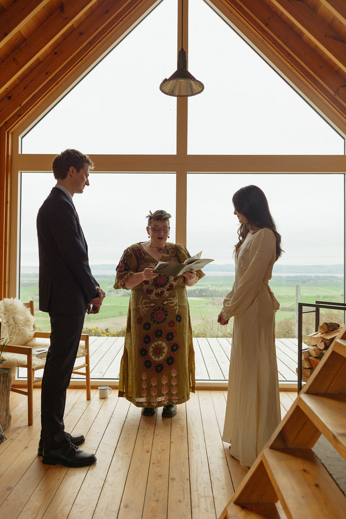 celebrant with patterned dress stands in between bride and groom conducting a humanist ceremony at guardswell farm