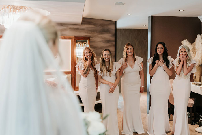 a line of bridesmaids wearing blush pink dresses looking at a bride 