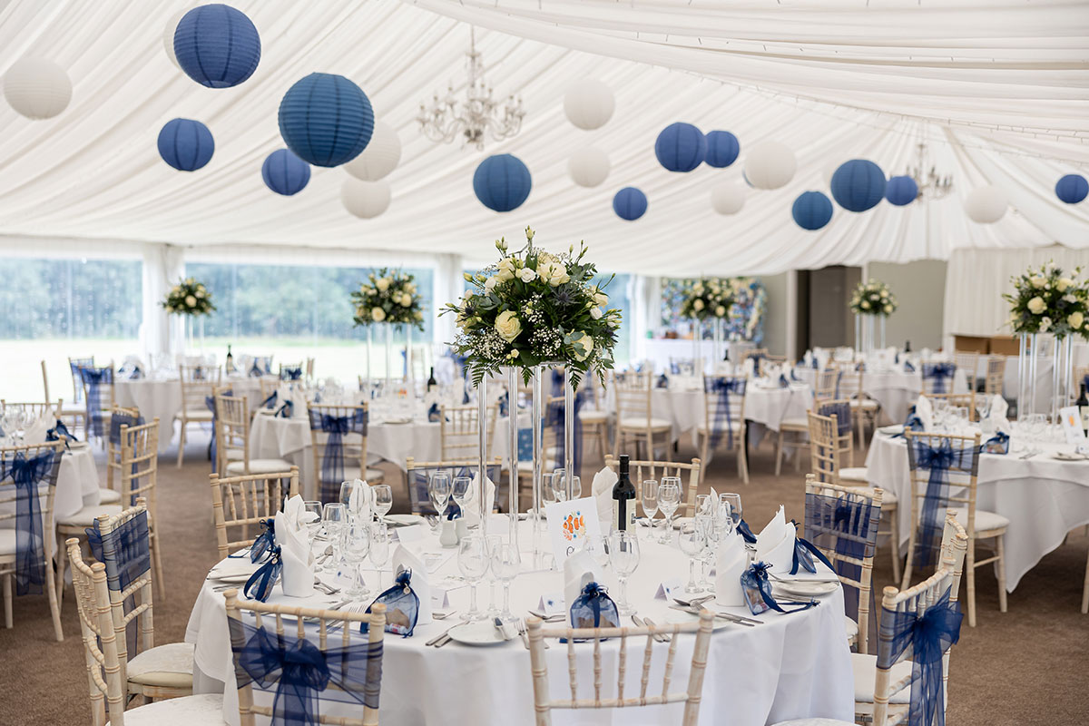 Wedding reception marquee at Melville Castle dressed with round tables, blue and white décor, floral centrepieces and draped ceilings