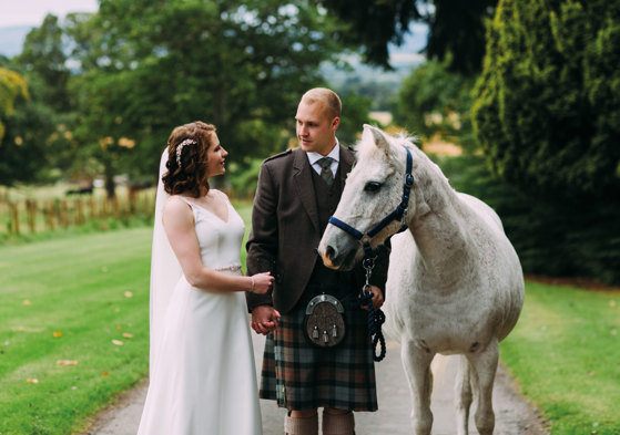 Bride and groom with white horse in grassland