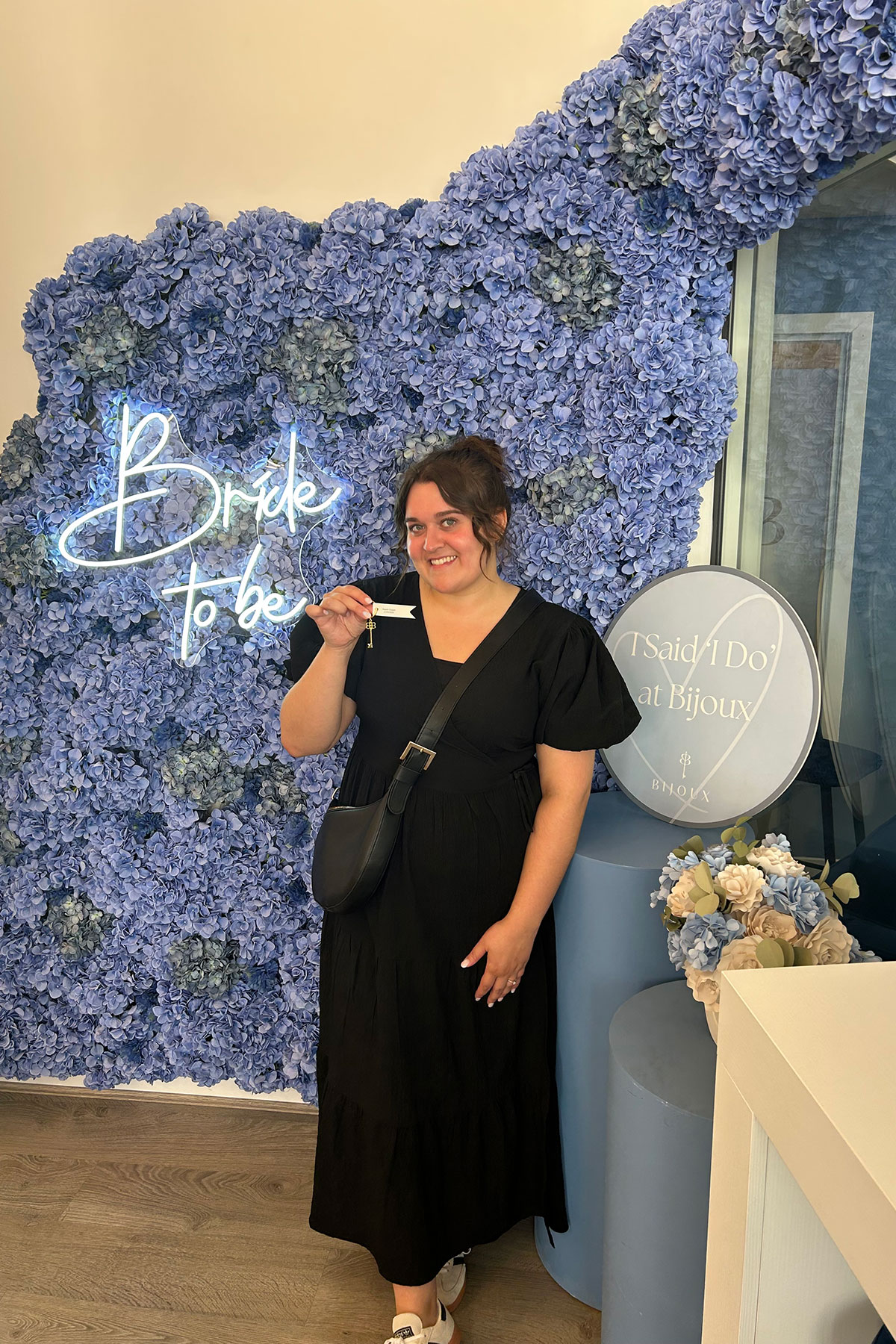 Bride-to-be at Bijoux Bridal posing with key in front of blue floral wall
