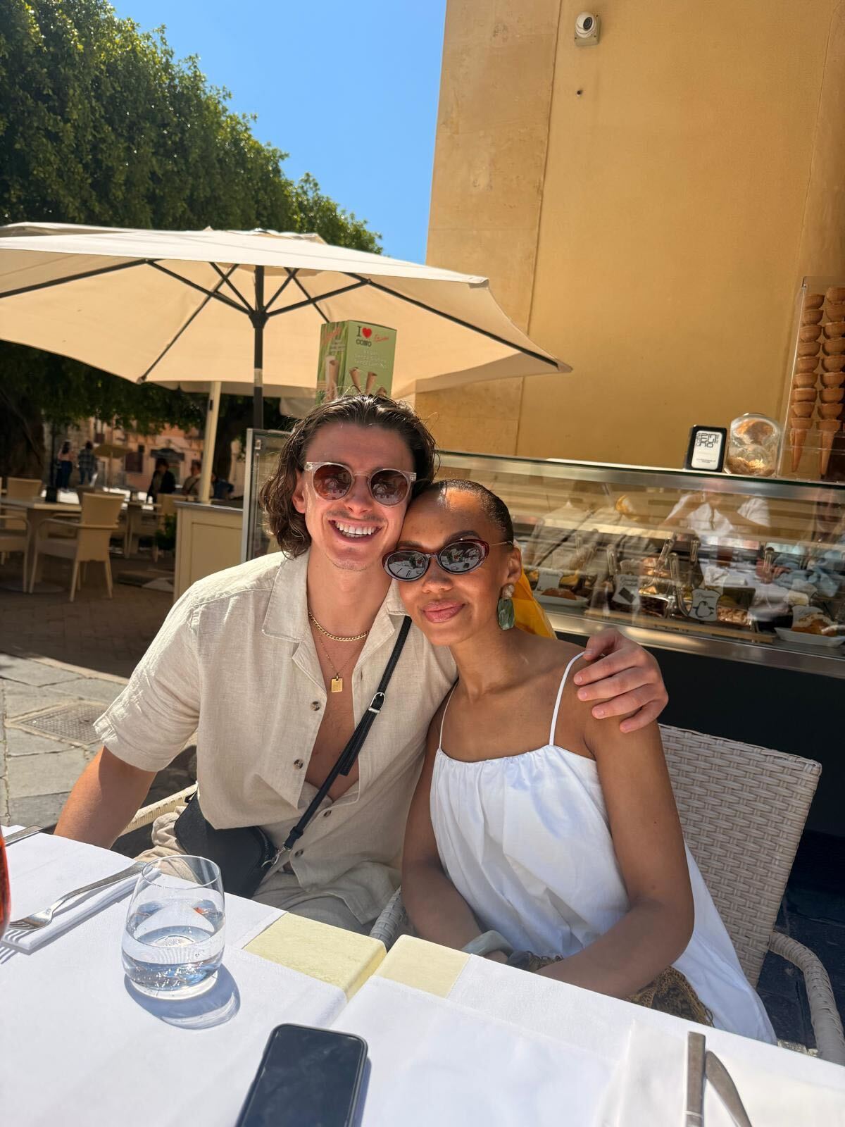 couple smile for a photograph on holiday with parasol in the background