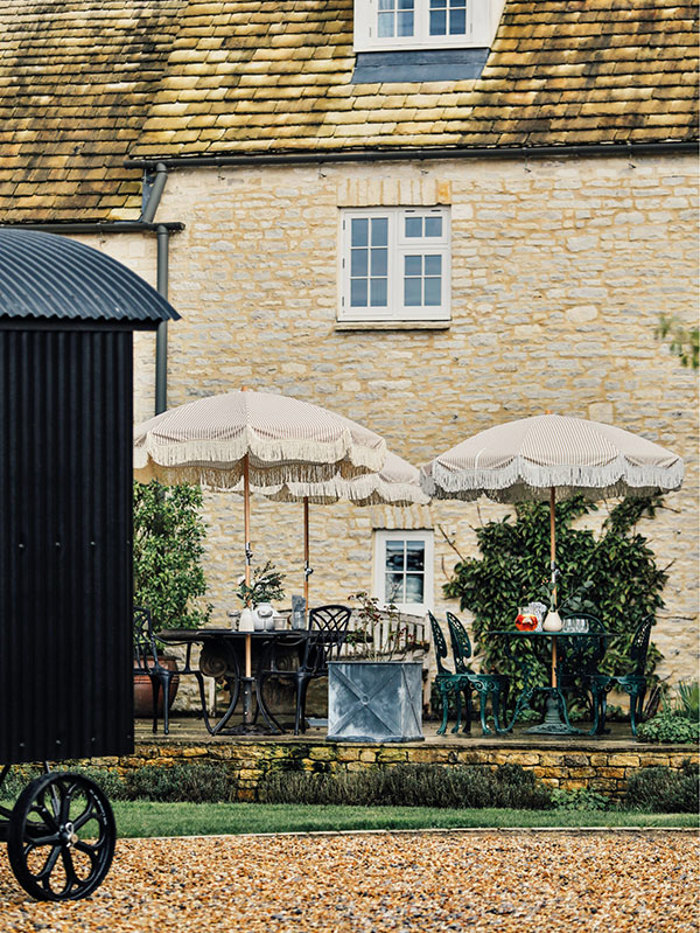 an outdoor display of two garden parasols and lawn furniture alongside a cobbled house