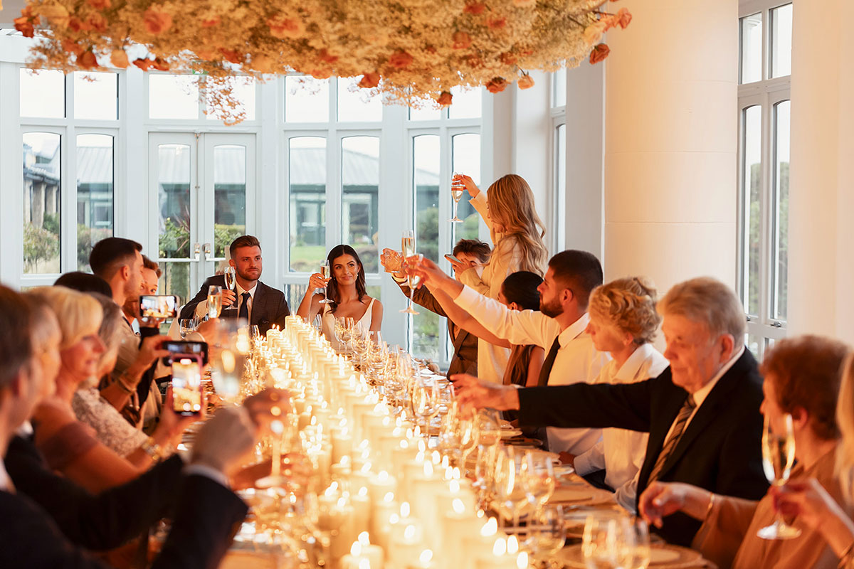 Wedding reception toast at Old Course Hotel St Andrews with long candlelit table and guests raising champagne glasses