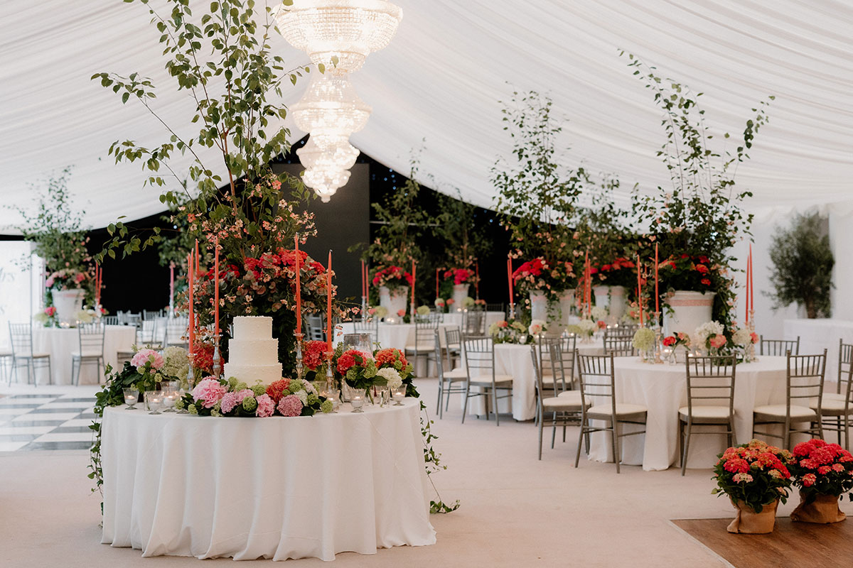 Tiered white wedding cake surrounded by colourful flowers and tall candles in the marquee at Mar Hall.