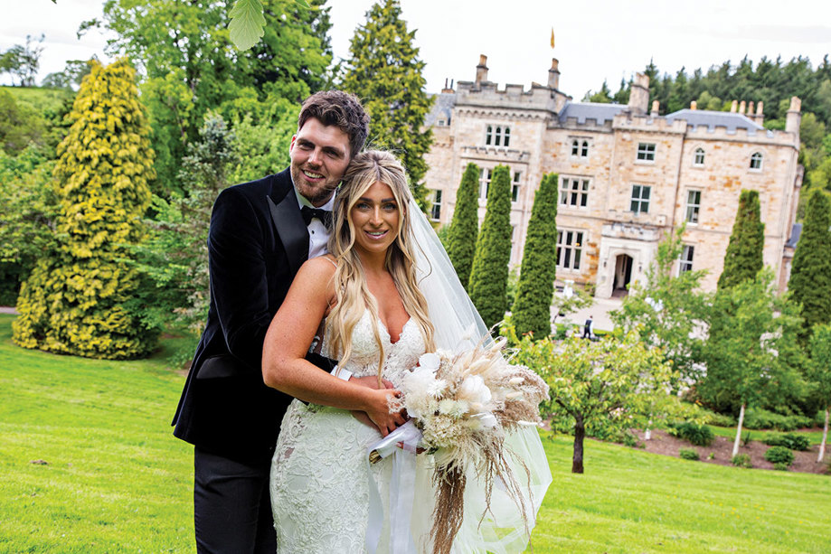 bride and groom smile for a photograph with crossbasket castle in the background