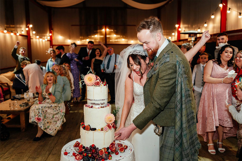 a couple cut a three tier wedding cake inside a barn