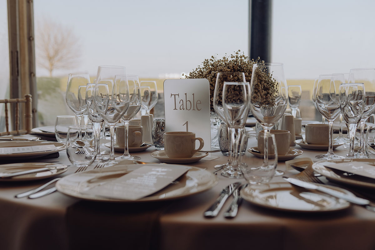 Wedding breakfast table at Ardoch Loch Lomond set with glassware, place settings, a floral centrepiece and countryside views through the windows.