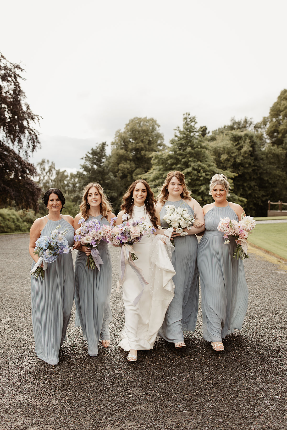 a bride with four bridesmaids wearing blue walking along a path at Netherdale House